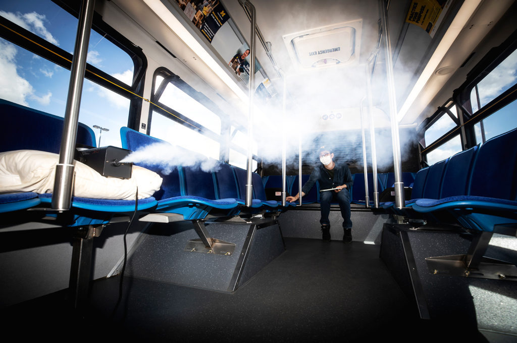 A man in a blue bus controlling a device releasing a spray.