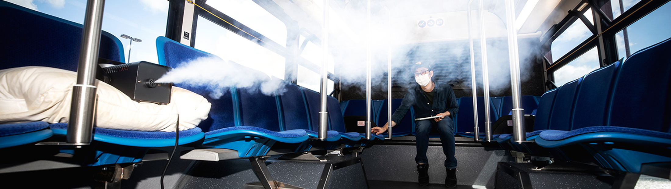 A man in a blue bus controlling a device releasing a spray.