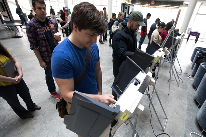 Several people in line to use a voting machine.