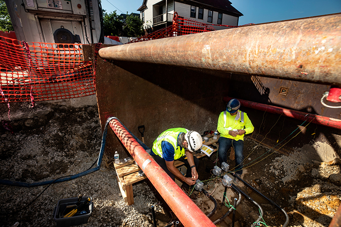 Image of Wentao Wang working with Great Lake Water Authority construction site workers to install sensors on a water pipe alteration in Detroit