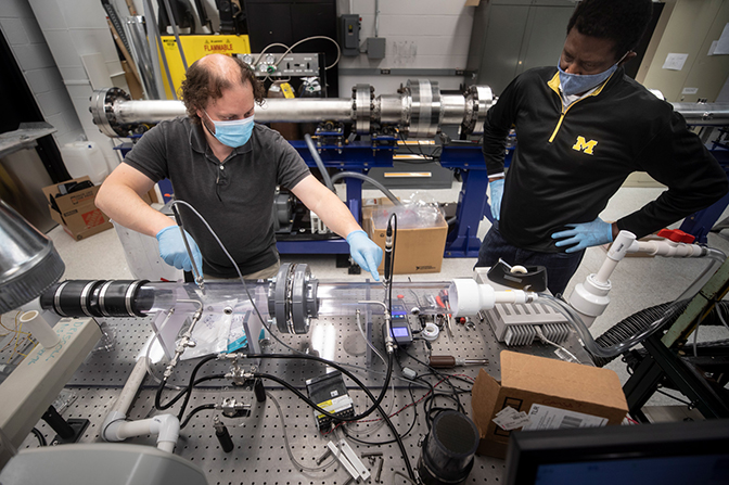 Image of Mirko Gamba and Herek Clack configuring a small wind tunnel to shoot particles at masks in order to test their protective capabilities after decontamination treatments