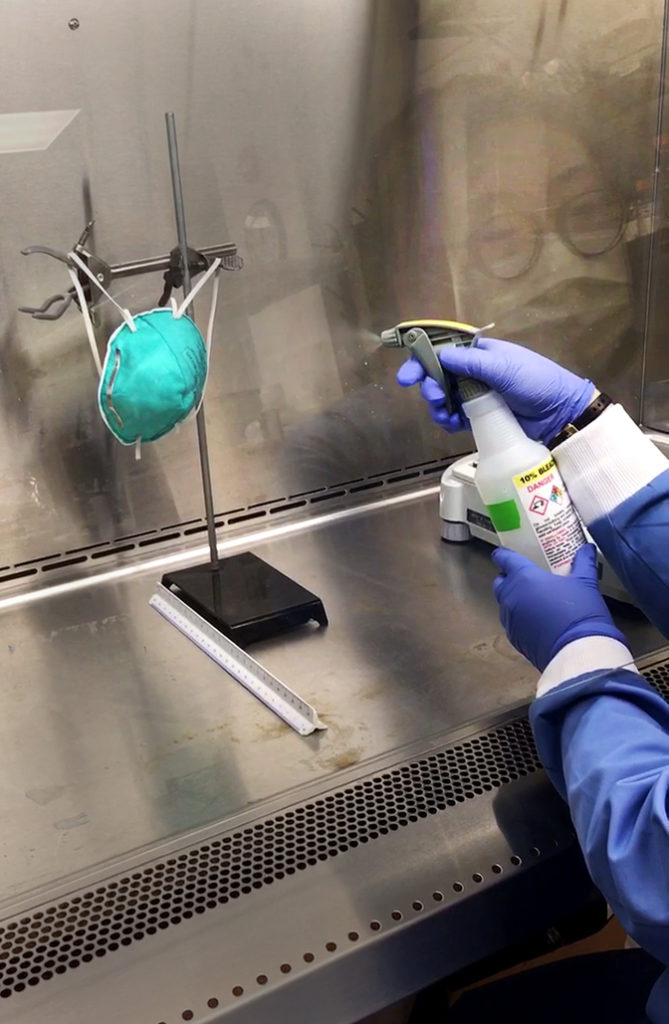 Image of Lucinda Li spraying an N95 mask with surrogate virus