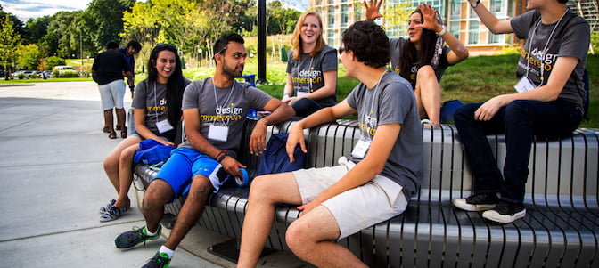 Group of students outside talking on a bench in the summer.