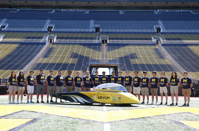 Students stand at the center of the Big House with Aevum on a sunny day