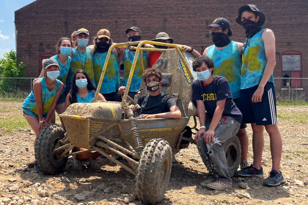 baja team around mud-cacked baja car