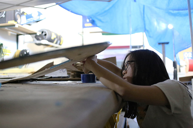 A girl working on a carbon fiber sheet on a workbench.