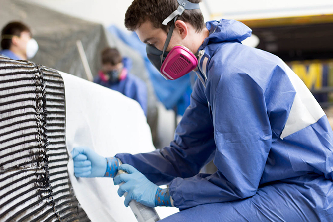 A student in a mask working on a carbon fiber material.