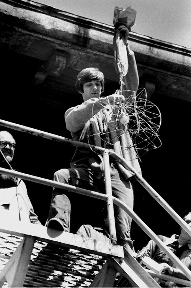 A person holds a contraption with an egg in the center over a railing.