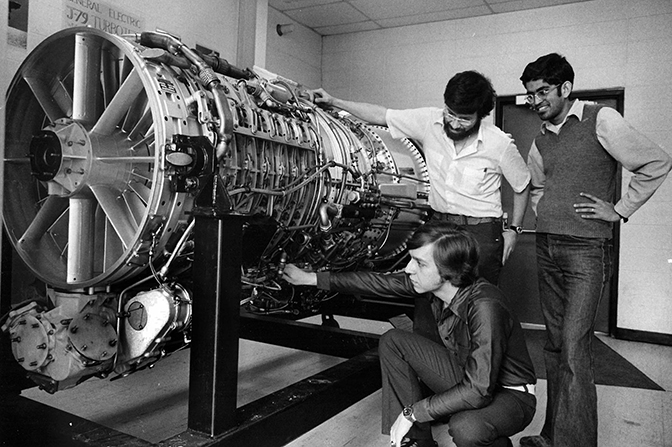 A black and white photo of three students examining a large engine.