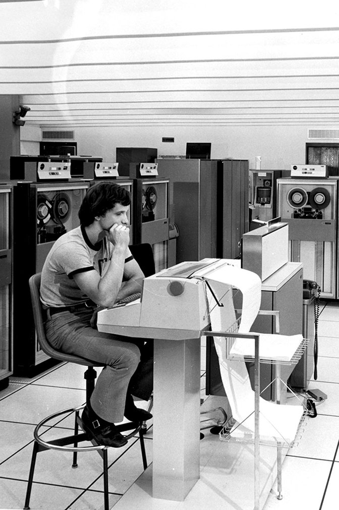 A man sitting at a device printing a long sheet of paper.