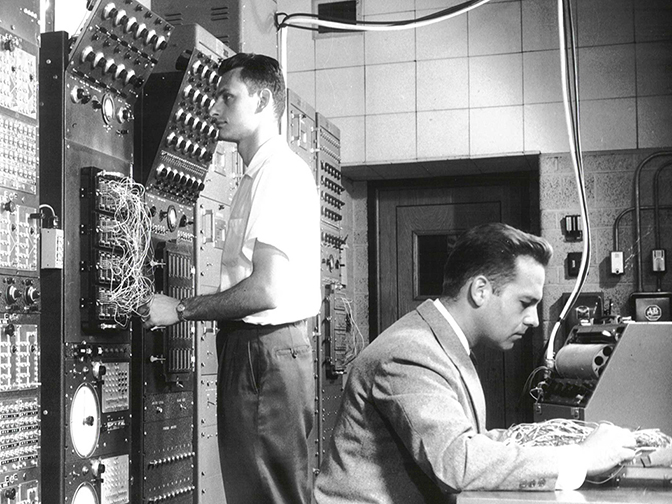 A black and white photo of two men working at a large computer.