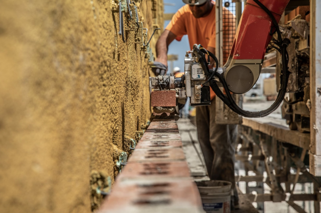A construction worker builds a brick wall with the help of a SAM, or Semi-Automated Mason. SAMs mortar and place bricks in exterior walls of large buildings.