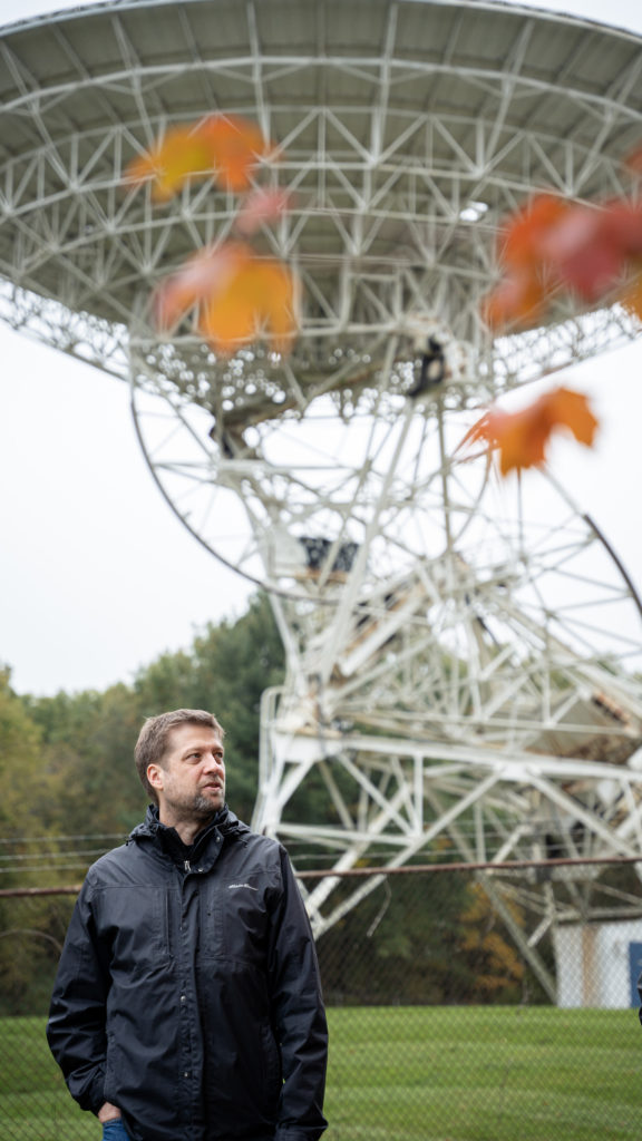 Jamie Cutler wears a black rain coat and stands outside the Dexter observatory. 
