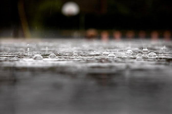 Close-up of raindrops splashing on a wet surface with blurred background.