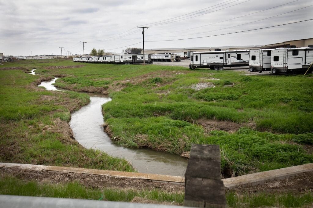 A drainage ditch with a small amount of water in it sits dozens of feet from an RV production lot