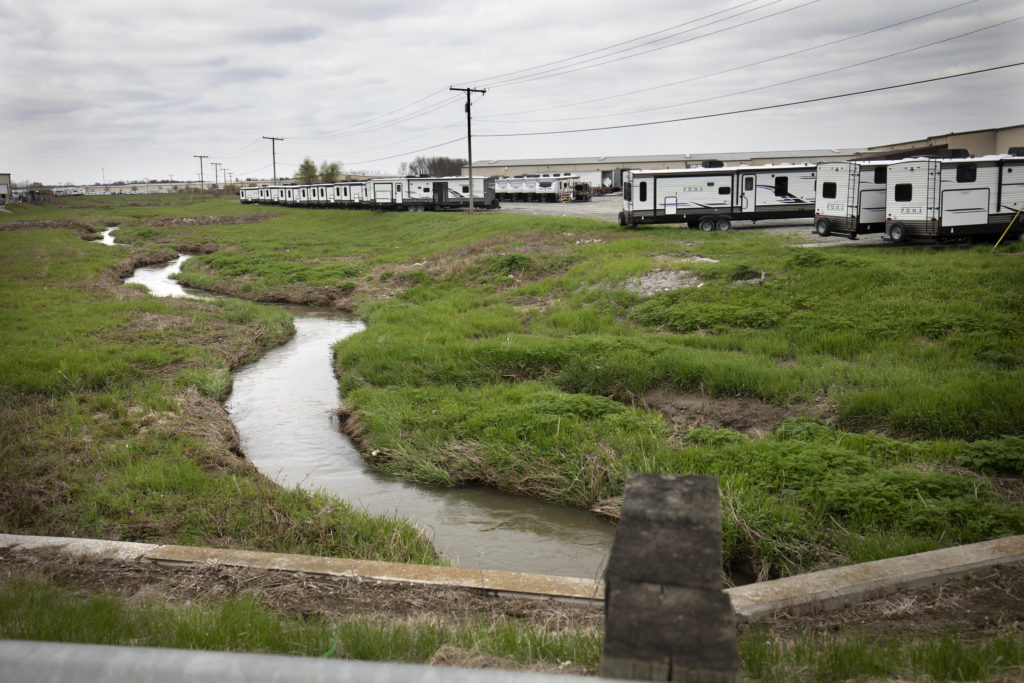 A drainage ditch with a small amount of water in it sits dozens of feet from an RV production lot