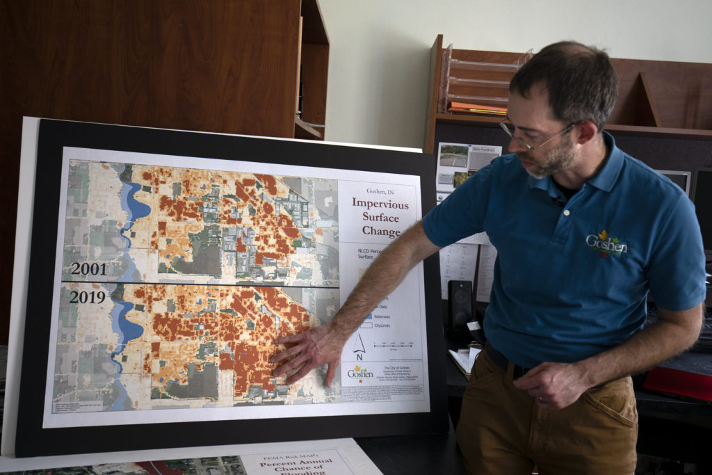 Kauffman, wearing a blue polo, stands pointing at a map showing major changes to the city over a 20 year period