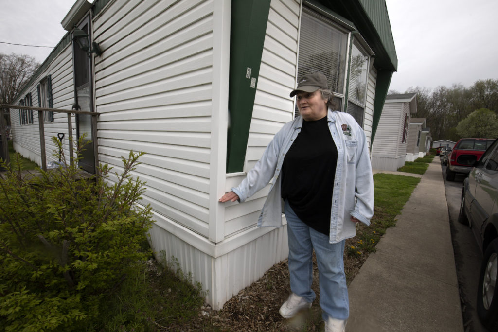 A woman stands next to her home with her hand signalling a 3ft water level from a previous flood