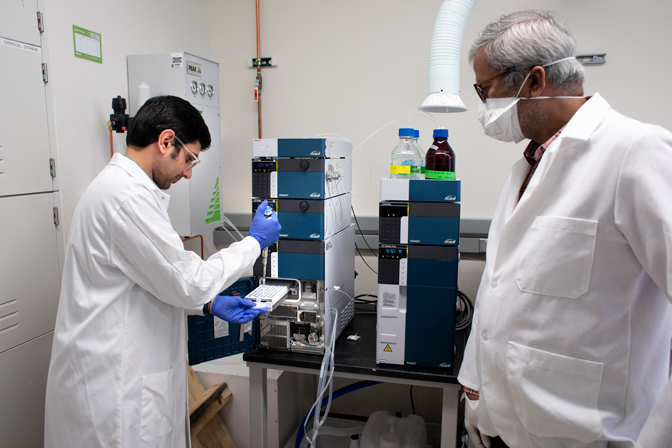 Two men in lab equipment stand in a lab talking