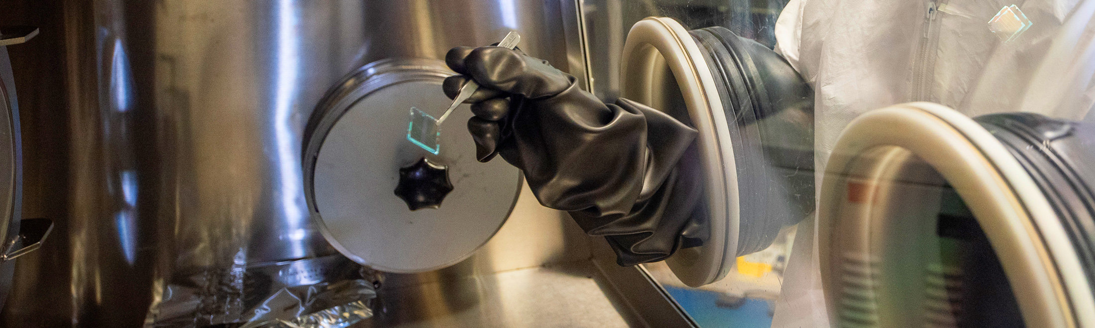 A gloved hand uses utensils to handle the photonics structure