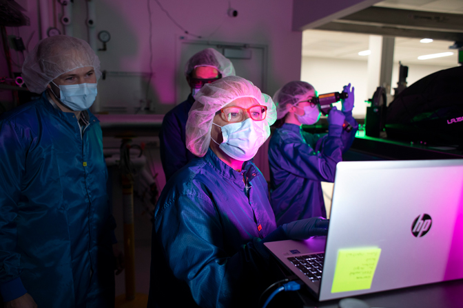 A group of people in lab gear gather around a computer