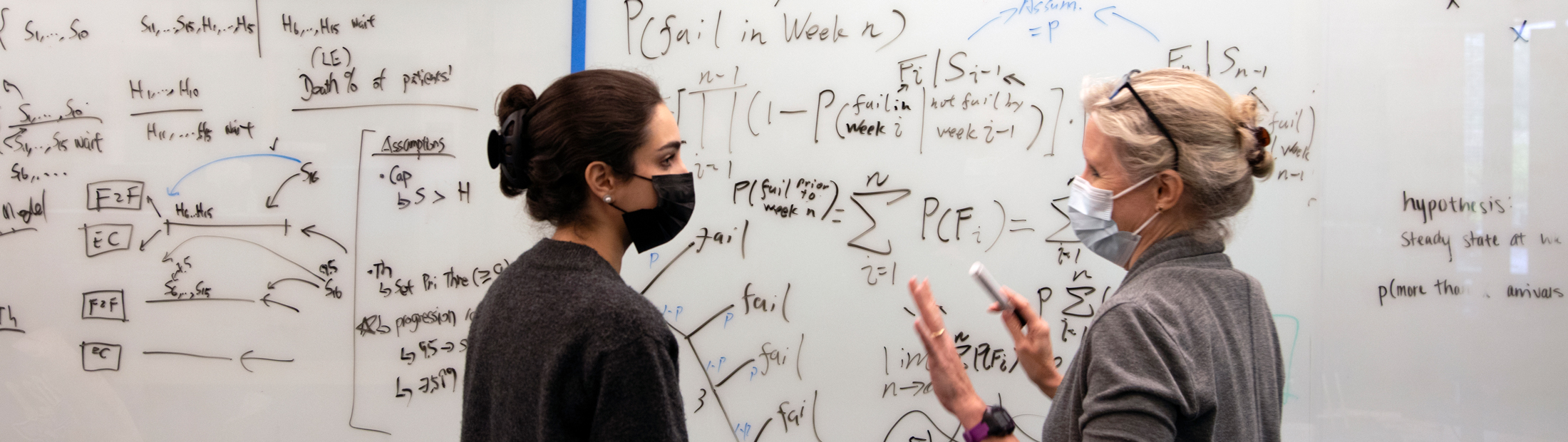 Amy Cohn talks with another researcher at a white board with equations on it