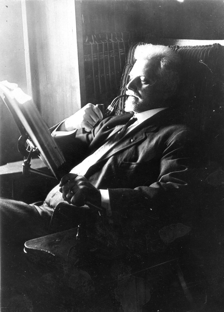 A black and white photo of a man reading and smoking a pipe