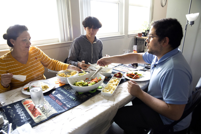 Díaz and his mother and brother sit around a table in an apartment serving themselves dinner with an assortment of dishes in the center of the table.