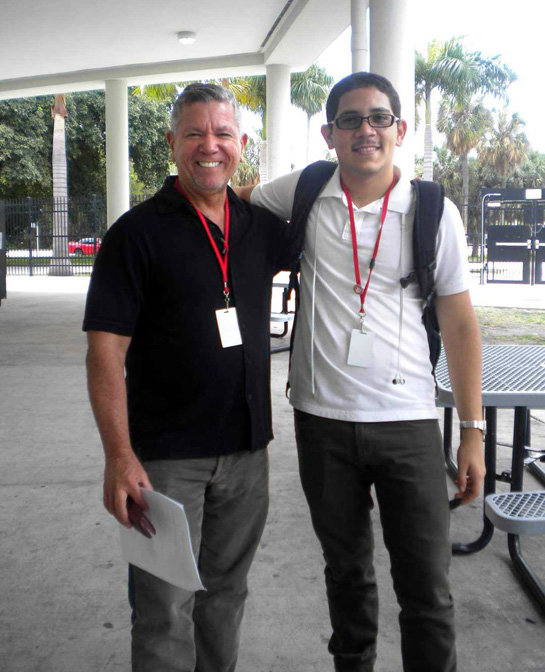 A high-school aged Díaz with his arm around his high school teacher on school grounds. Both are wearing lanyards.