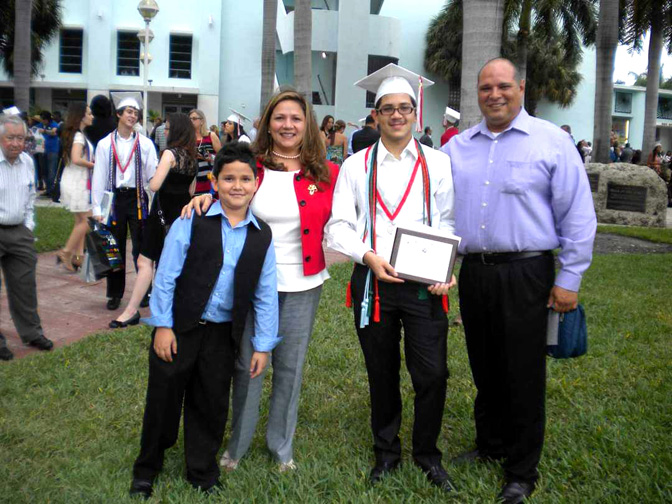 A high-school aged Díaz wearing graduation cords and a cap while holding a diploma and standing between family members.