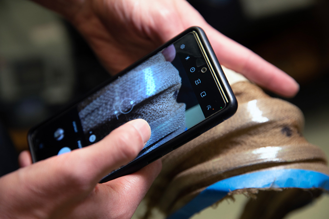 Brian Iezzi use his phone to simulate the scanning of the photonic fibers fabric he developed. In the future, one will be able to use their phone to read the clothing woven-in labels made with inexpensive photonic fibers. 