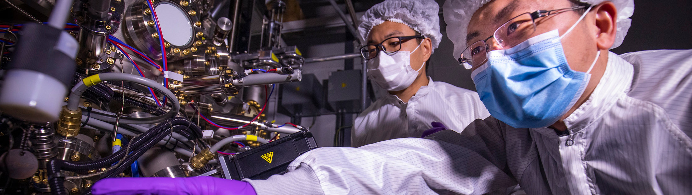 Research scientists Ding Wang (left) and Ping Wang (right) discuss the growth behavior of the ferroelectric semiconductor deposited using the molecular beam epitaxy system that is visible on the left.