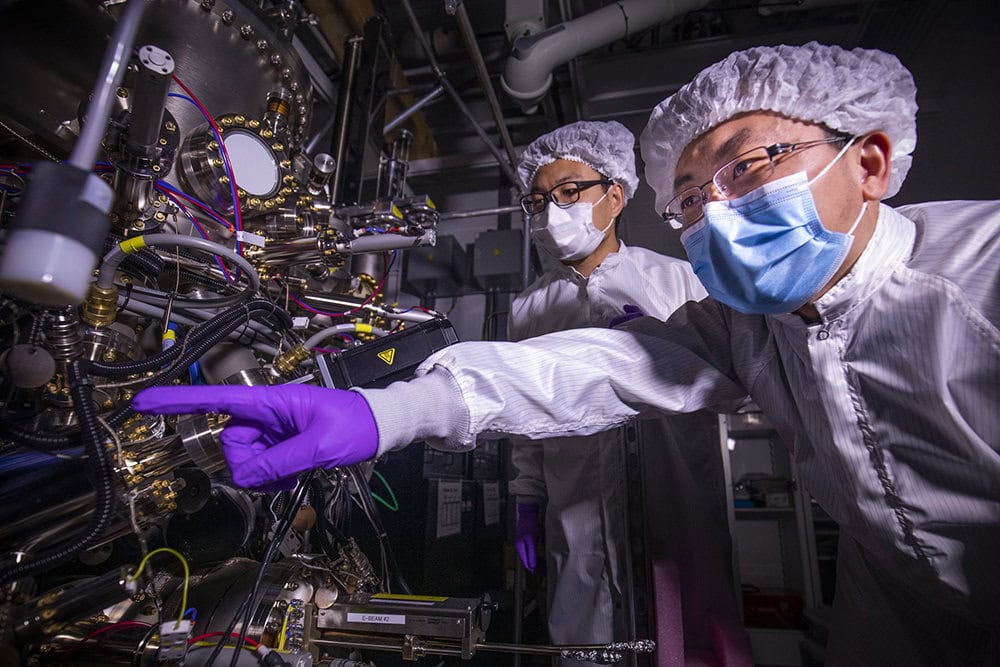 two researchers in PPE and purple gloves examining a large piece of lab equipment