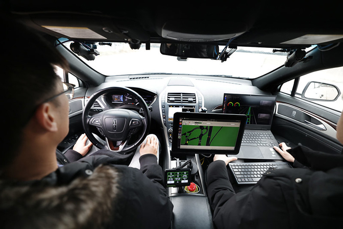 Two researchers sit in a car filled with tech and screens to monitor their driving and simulate fake cars around them