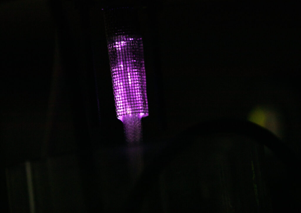 A close-up of plasma in the reactor. The photo is dark but you can see purple light emanating from the reactor.