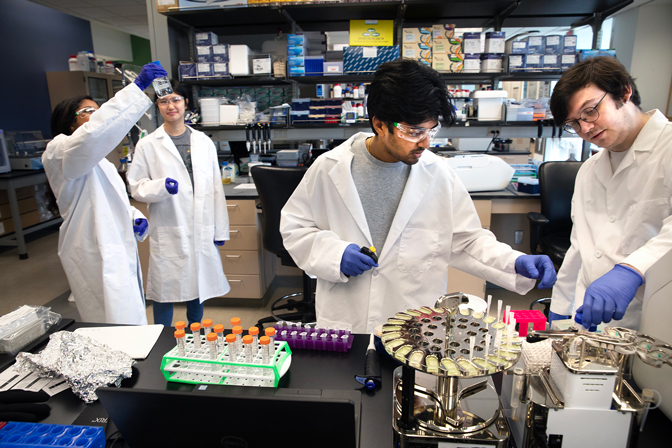 Four students wearing lab equipment using bits of equipment around the room
