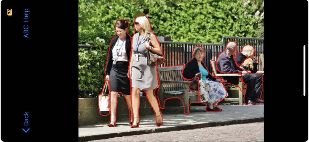 The screenshot shows two women in business dress in the foreground of the photo, and two park benches in the background. One bench has an older woman sitting on it, facing the camera, and the other has two older men who are looking away. ImageExplorer identifies all these in red outline. The wall of greenery, fence, sidewalk and street are not outlined.