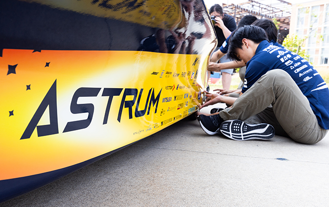 Ethan Lei sits on the ground next to the Astrum solar car