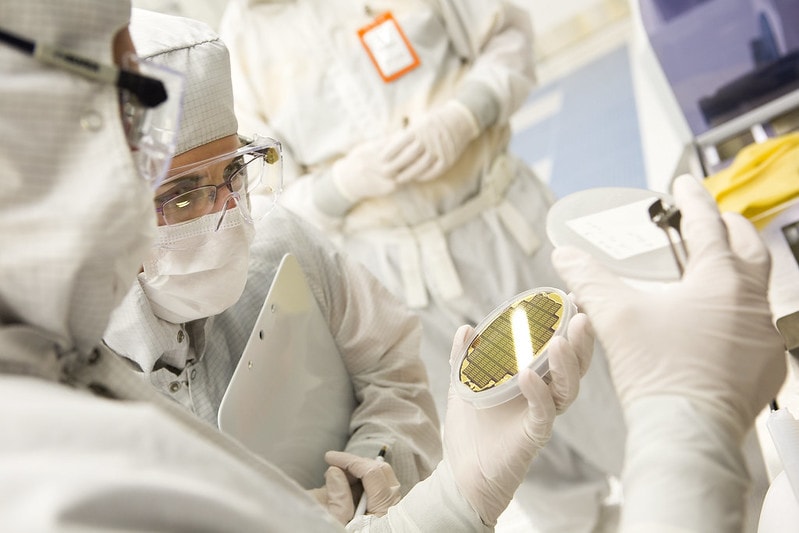 People wearing lab equipment, including masks and goggles, closely examine a chip plate.