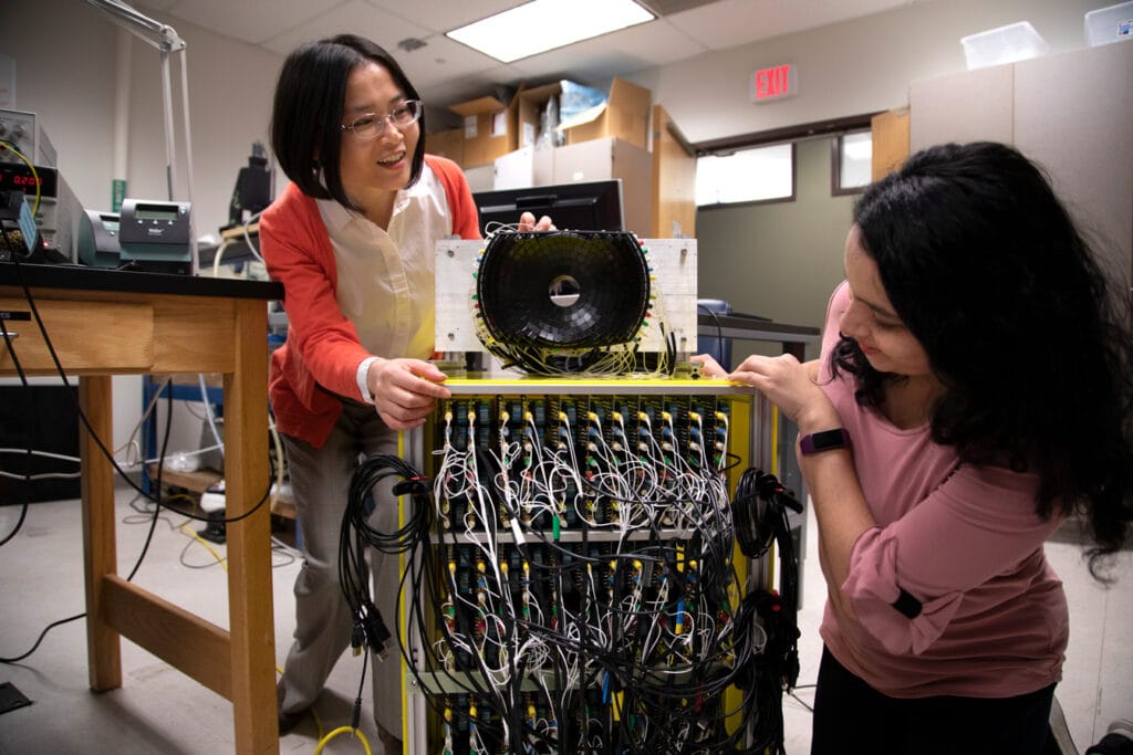 Two researchers adjust a complex looking device with many rows and columns of wires