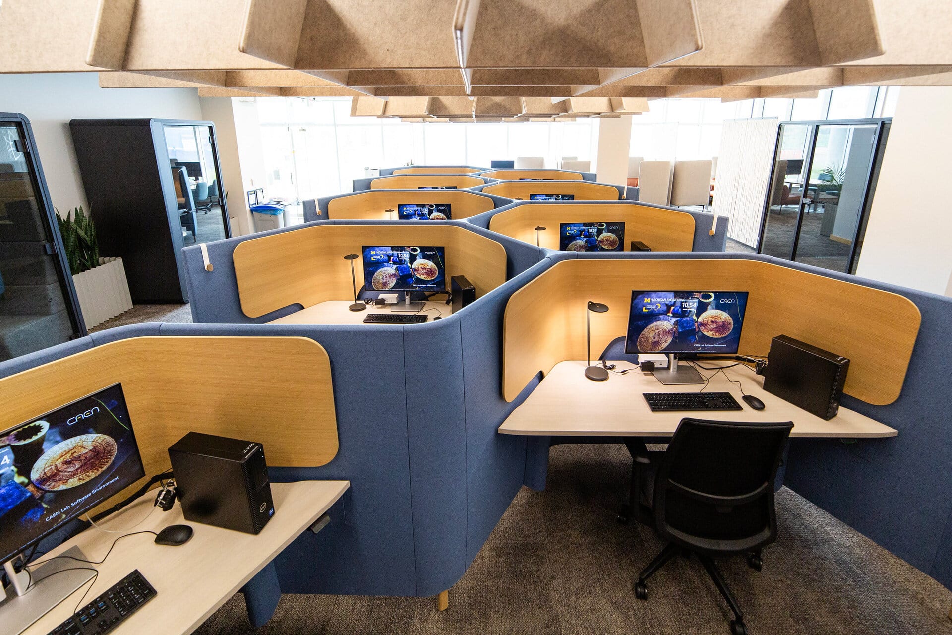 A view of the new Quiet Space lab. There are many computers at desks with dividers. There are also quiet pods around the room.