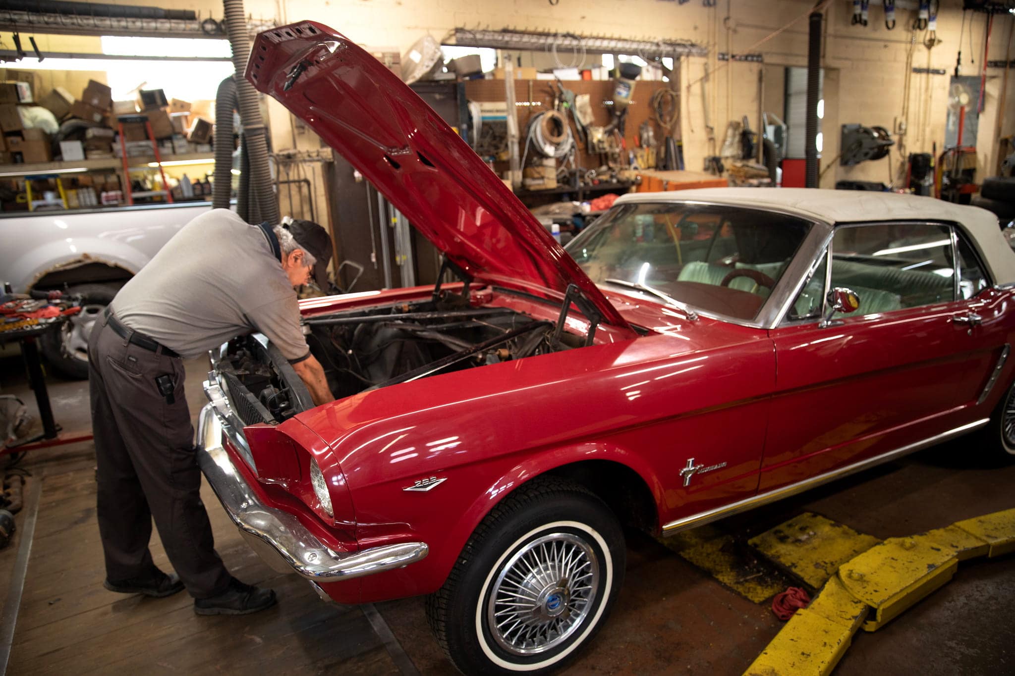 An elderly man leans over the hood of a cherry red Mustang