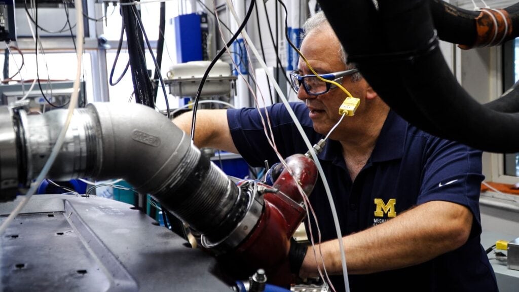Andre Boehman wears safety goggles and adjust an instrument in the lab