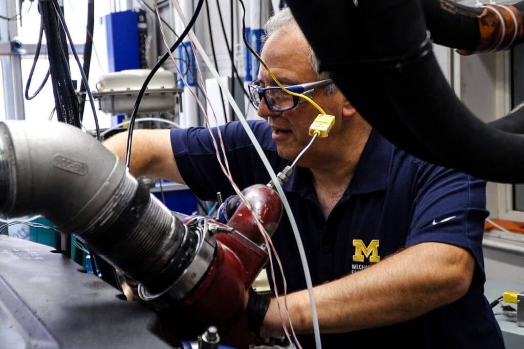 Andre Boehman wears safety goggles and adjust an instrument in the lab