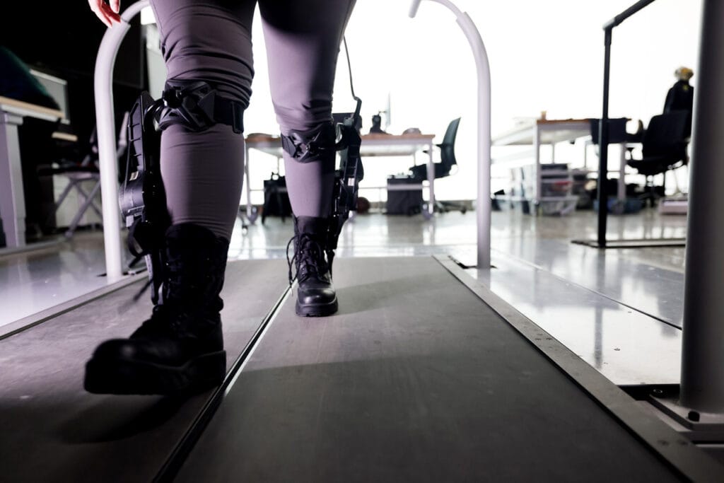 A close up shot of a person walking on a treadmill. Below the knees, the exoskeleton helps the wearer walk more efficiently.