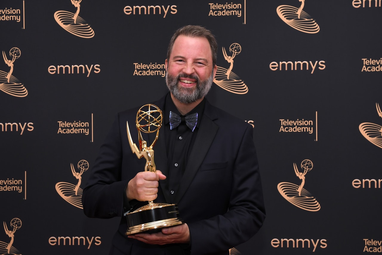 Paul Debevec stands in front of a black background with the Emmy television academy awards logo patterned throughout, holding an academy award and smiling.