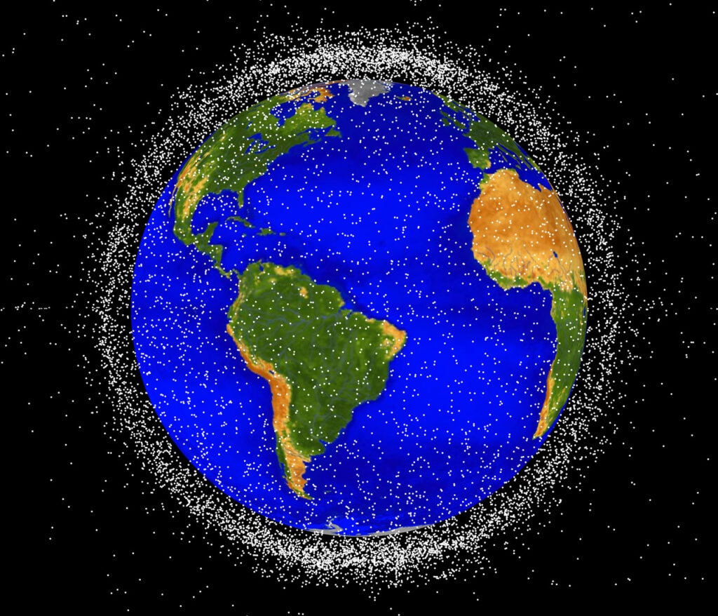 The space junk appears as many small white points surrounding Earth, which has bright blue oceans and green and brown continents. The space junk is thick enough to form a cloud that obscures most of the black background when viewed from the edges around Earth.