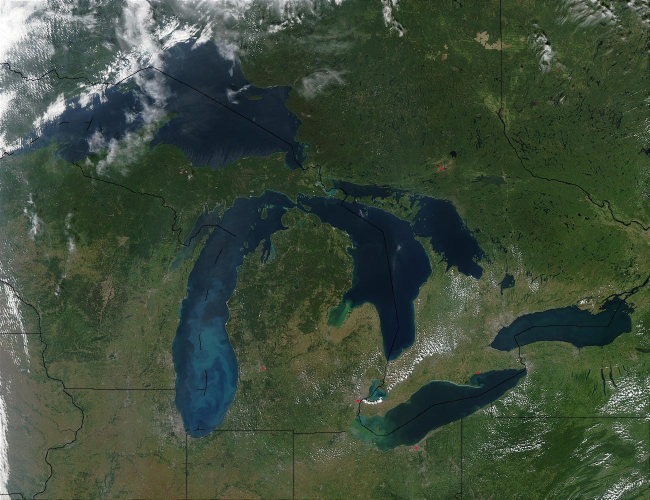 Satellite image of the state of Michigan and the surrounding states. Lake Superior covers the upper left corner. Beneath it is Lake Michigan, and to the right is Lake Huron. Under Lake Huron is Lake Erie (left) and Lake Ontario (right). The pale blue swirls in Lake Michigan are probably caused by a phytoplankton bloom or calcium carbonate (chalk) from the lake's limestone floor. Concrete-grey patches mark the locations of several cities throughout the Great Lakes region. Red dots indicate active fire locations.