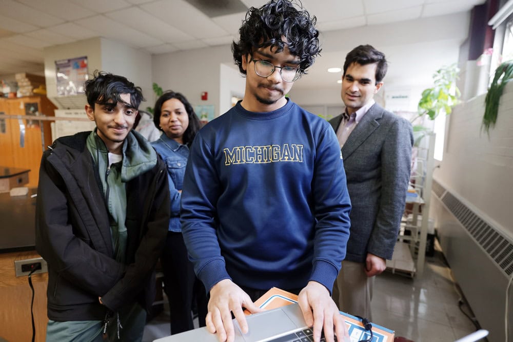 Mohammed Miah types on a laptop inside their chemistry classroom. Saleh, Akhavan-Tafti and Soni watch from behind.