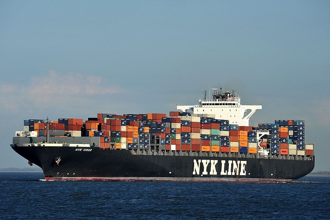 An ocean containership stacked with shipping containers of various colors, in the ocean.